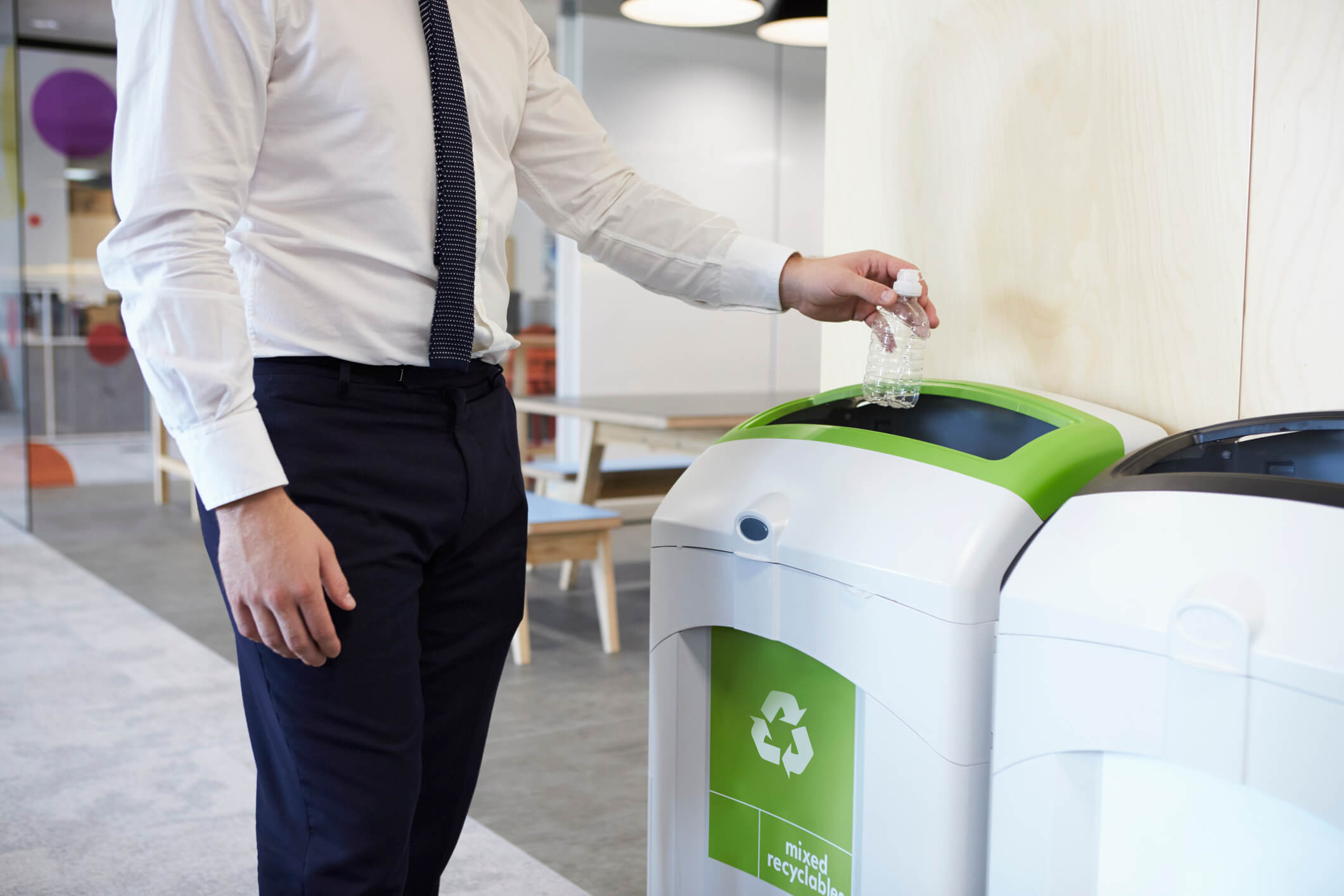 Man placing plastic bottle in recycle bin in office